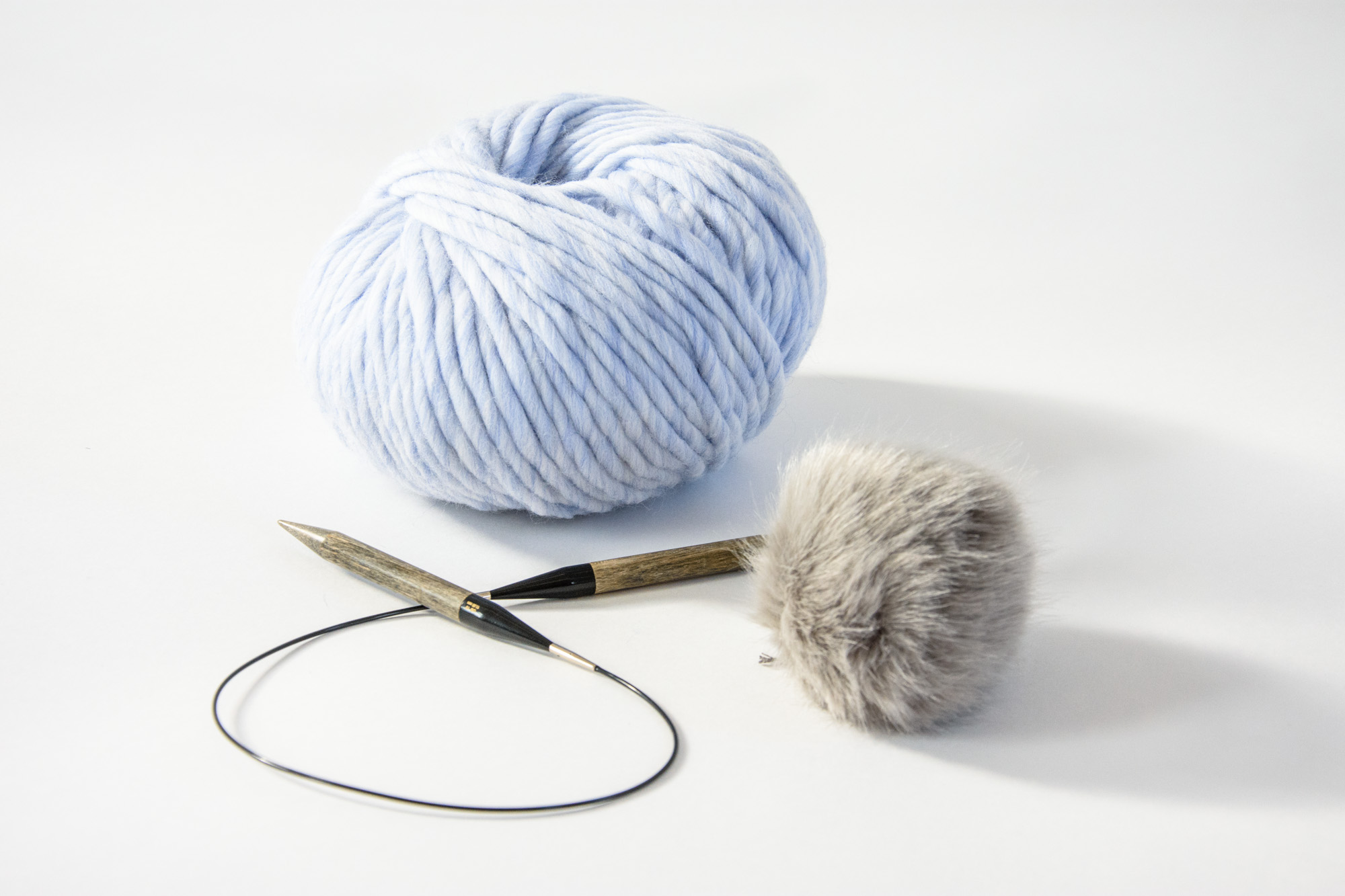 circular knitting needles with super chunky yarn and a faux fur pom pom