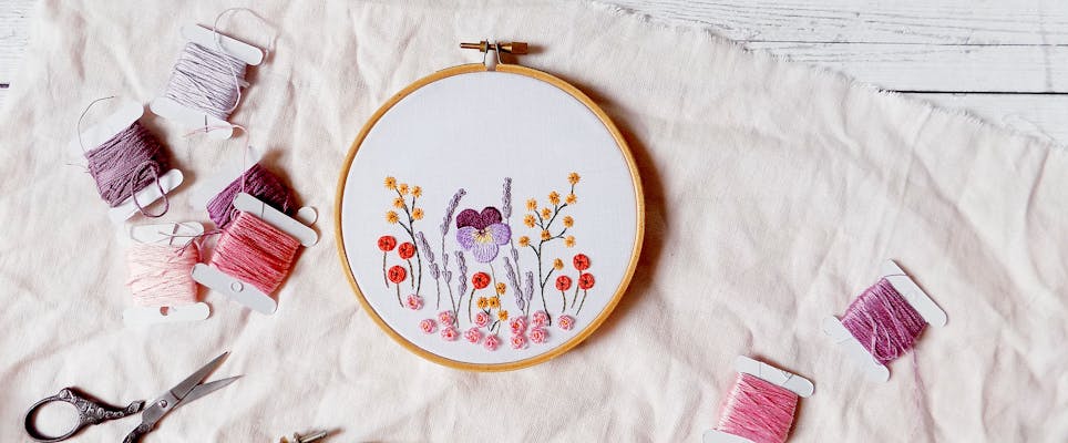 Embroidered flowers on white fabric on a hoop, with embroidery thread and scissors scattered around