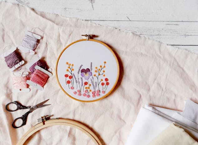 Embroidered flowers on white fabric on a hoop, with embroidery thread and scissors scattered around