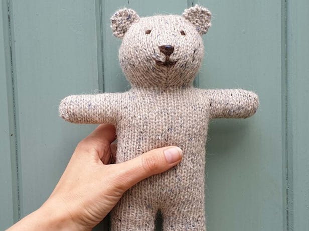 Hand holding a brown knitted teddy bear