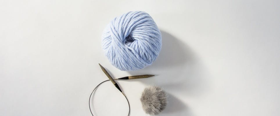circular knitting needles with super chunky yarn and a faux fur pom pom