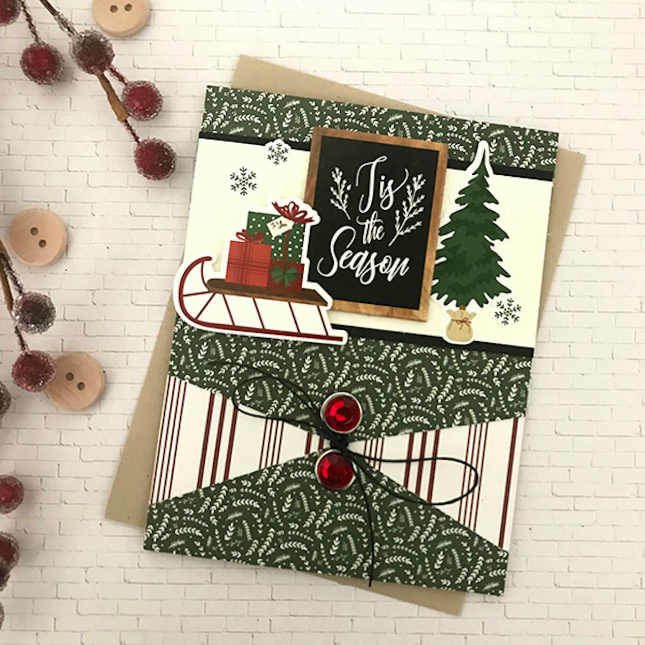 "tis the season" christmas card with small sleight of presents and a tree as well as a envelope-like fold with a ribbon tie