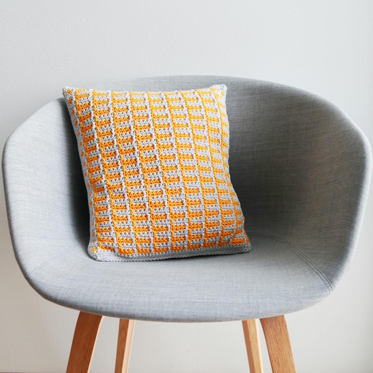 Mosaic Crochet Cushion with Geometric Shape sitting in a grey chair