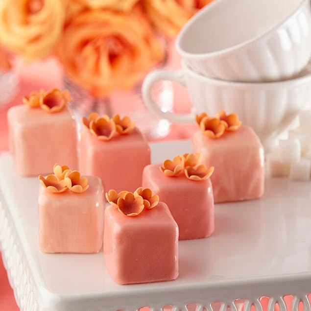 Petit fours covered with pink candy melts and decorated with small orange flowers