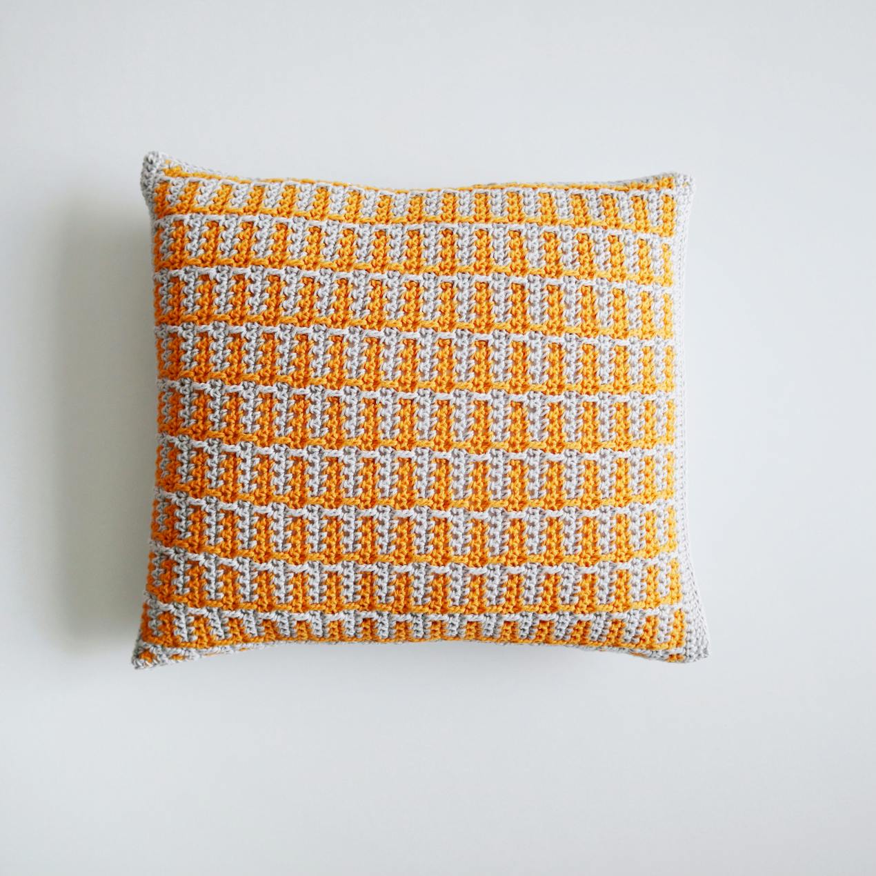 Mosaic Crochet Cushion with a geometric pattern in yellow and grey laying flat on a white background