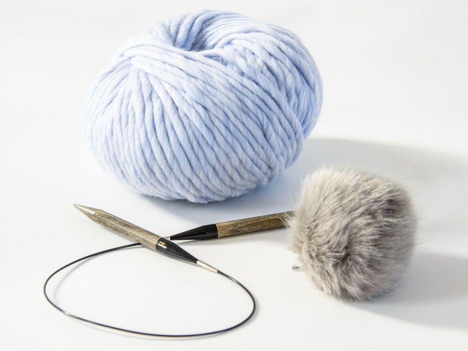 circular knitting needles with super chunky yarn and a faux fur pom pom