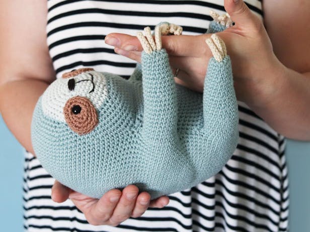 Amigurumi sloth handing from a person's hand