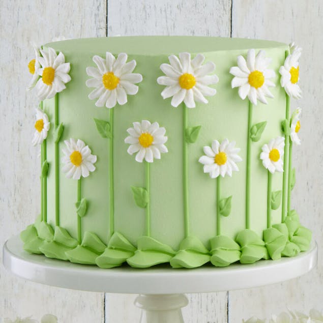 Round cake frosted in light green with daisies along the sides