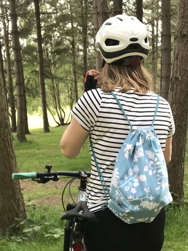 Woman wearing a striped t shirt, bike helmet and a drawstring bag with her back to the camera next to a bike